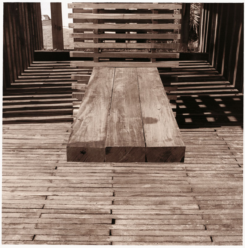 La mesa está formada por tres tablones de madera. No tiene patas sino que se mantiene empotrada en una subestructura, también de madera, que funciona como una palanca.
